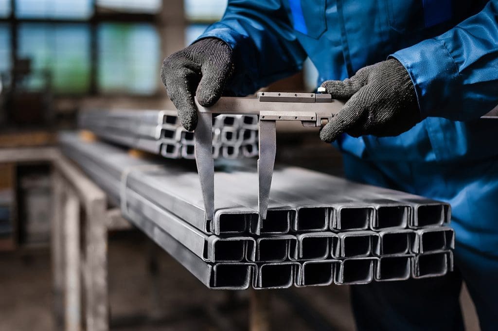 a metalworker uses a set of calipers to measure steel beams